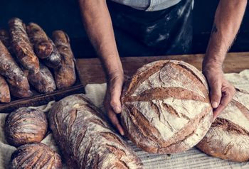 manos de panadero muestra pan redondo junto a otras variedades sobre mesa